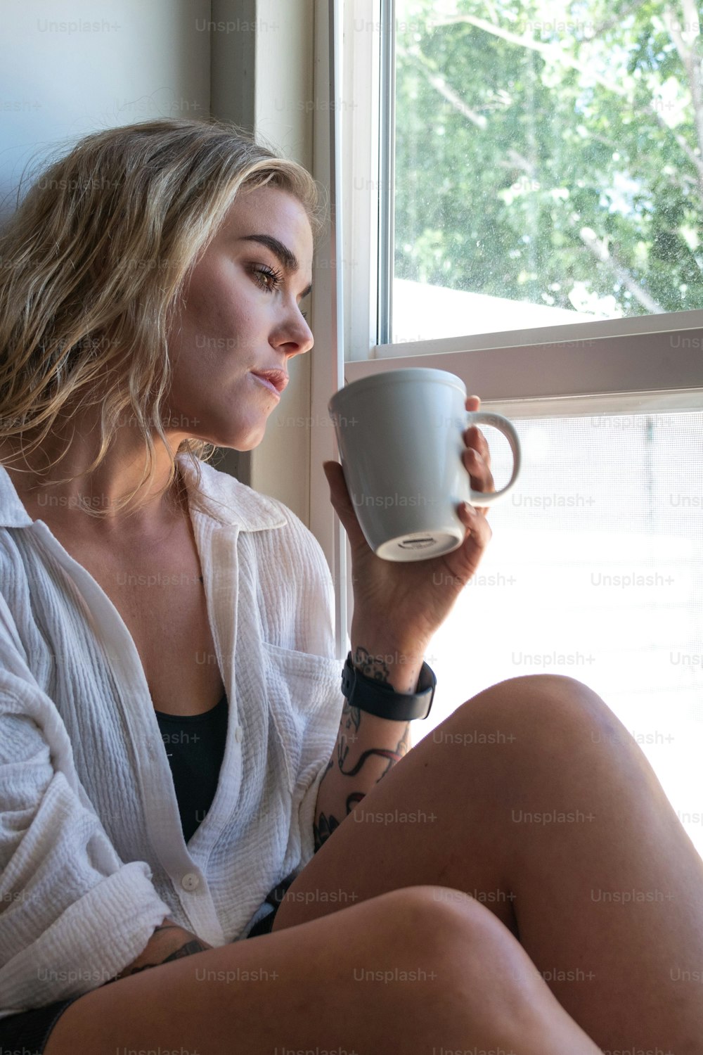 uma mulher sentada no peitoril de uma janela segurando uma xícara de café