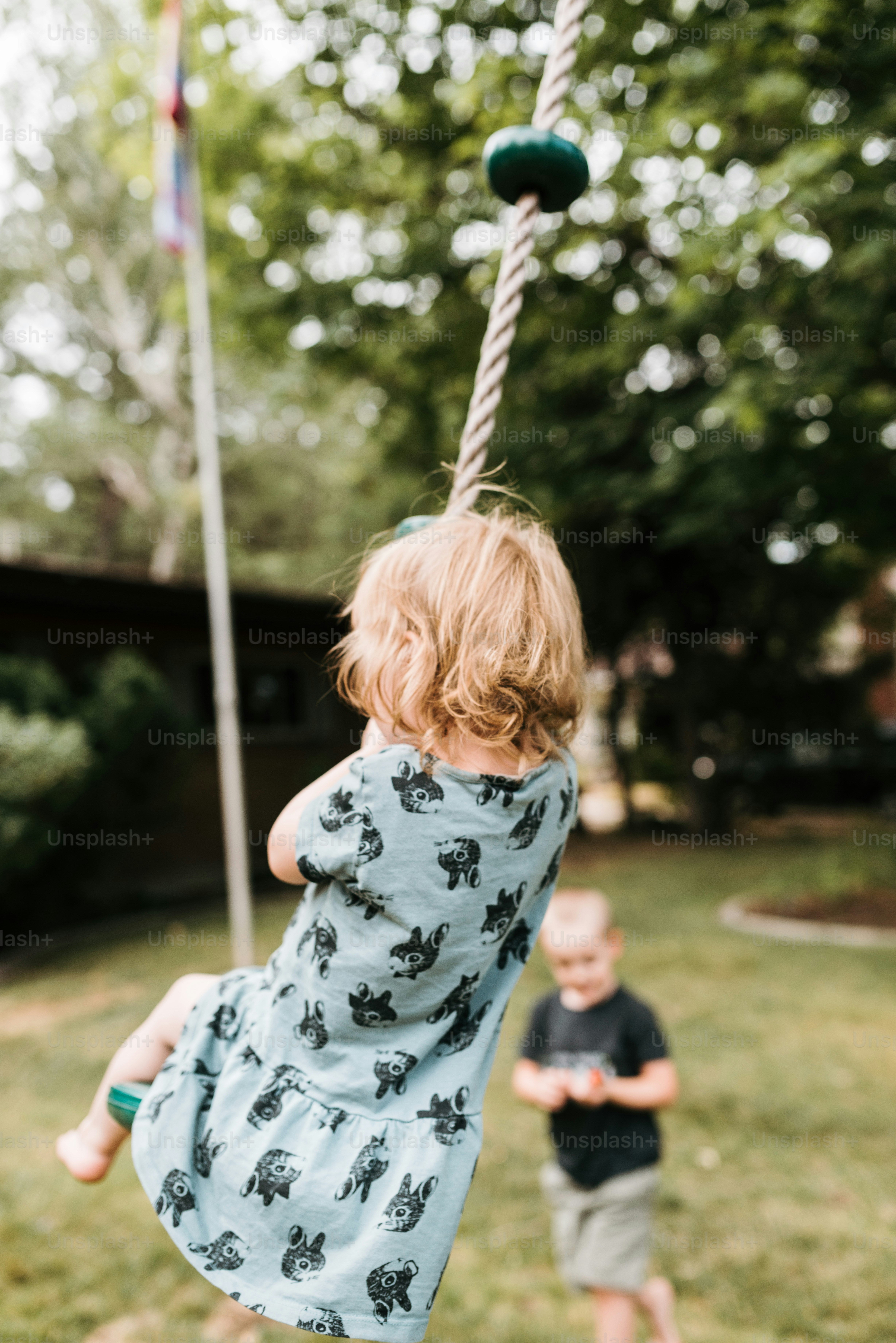 a little girl swinging on a rope next to a little boy