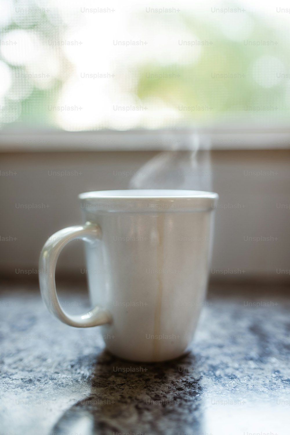 a steaming cup on a table in front of a window