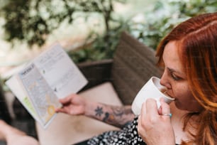 a woman sitting at a table reading a book and drinking a cup of coffee