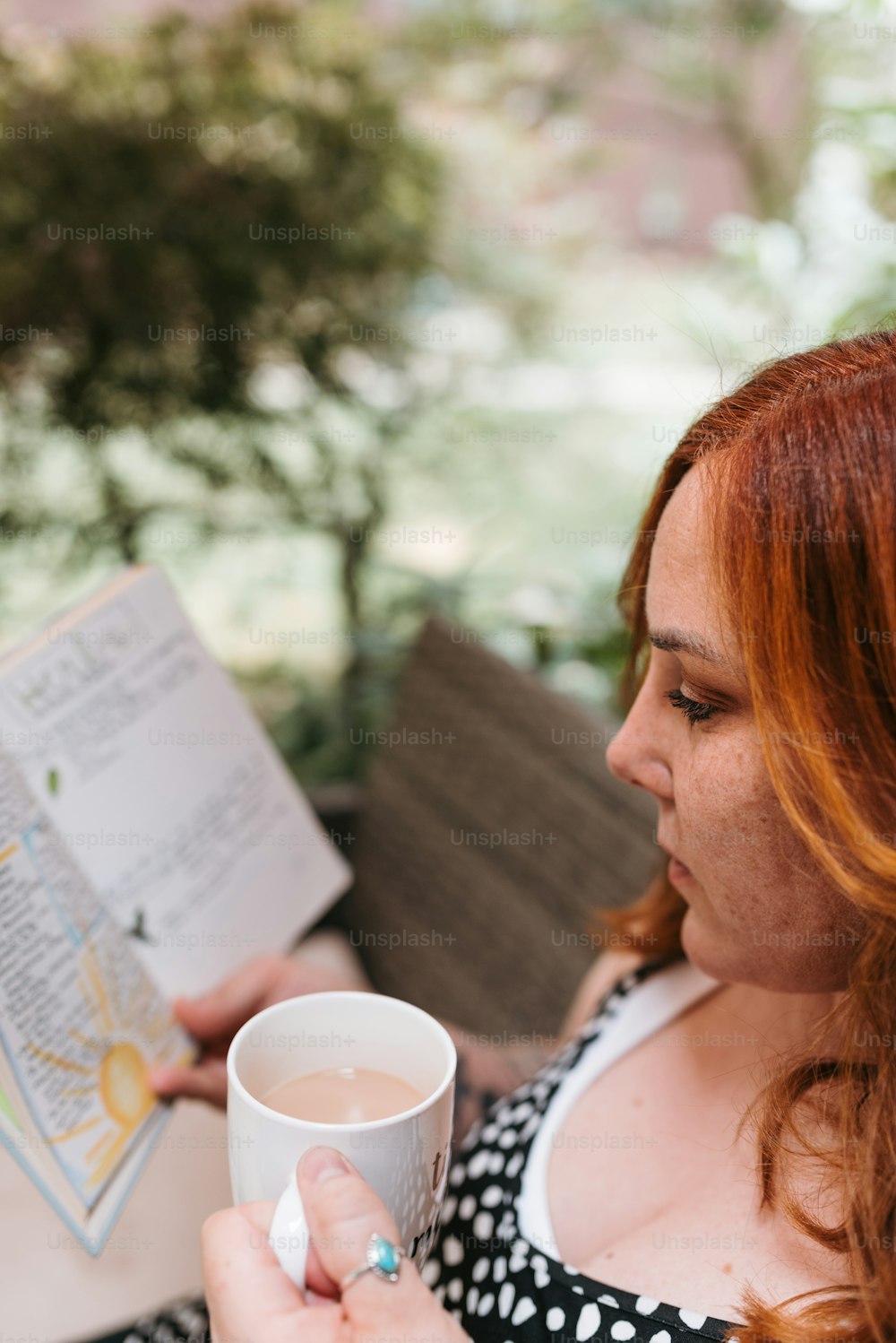uma mulher lendo um livro e segurando uma xícara de café