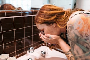 Eine Frau mit roten Haaren, die Wasser aus einem Wasserhahn trinkt