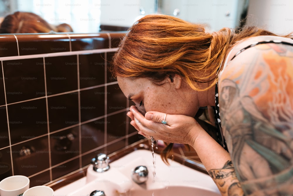 a woman with red hair drinking water from a faucet