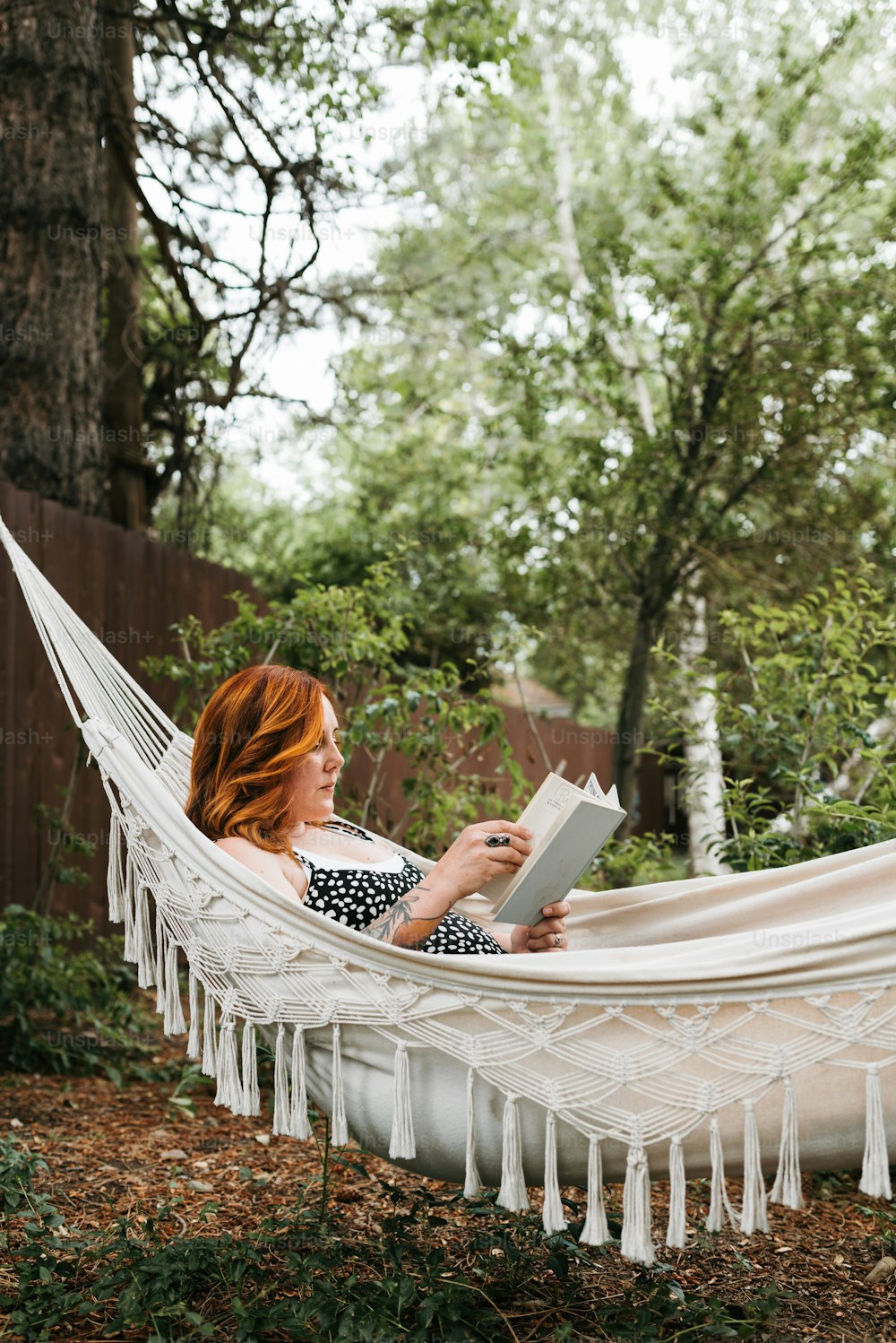 a woman sitting in a hammock reading a book
