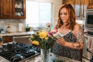 a woman standing in a kitchen with flowers in a vase