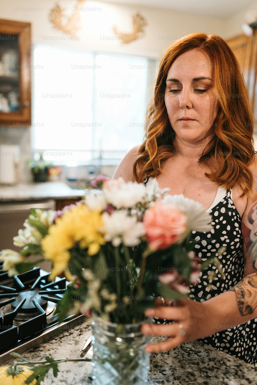 a woman arranging flowers in a vase on a kitchen counter