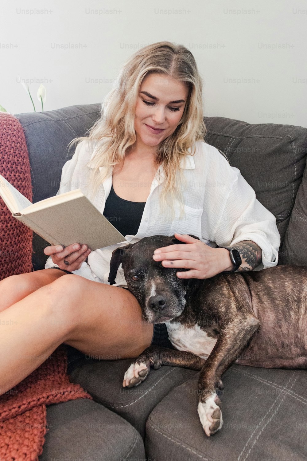 uma mulher sentada em um sofá lendo um livro com seu cachorro