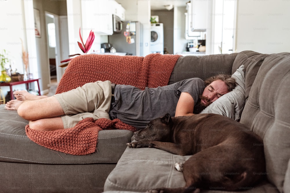 a man sleeping on a couch next to a dog