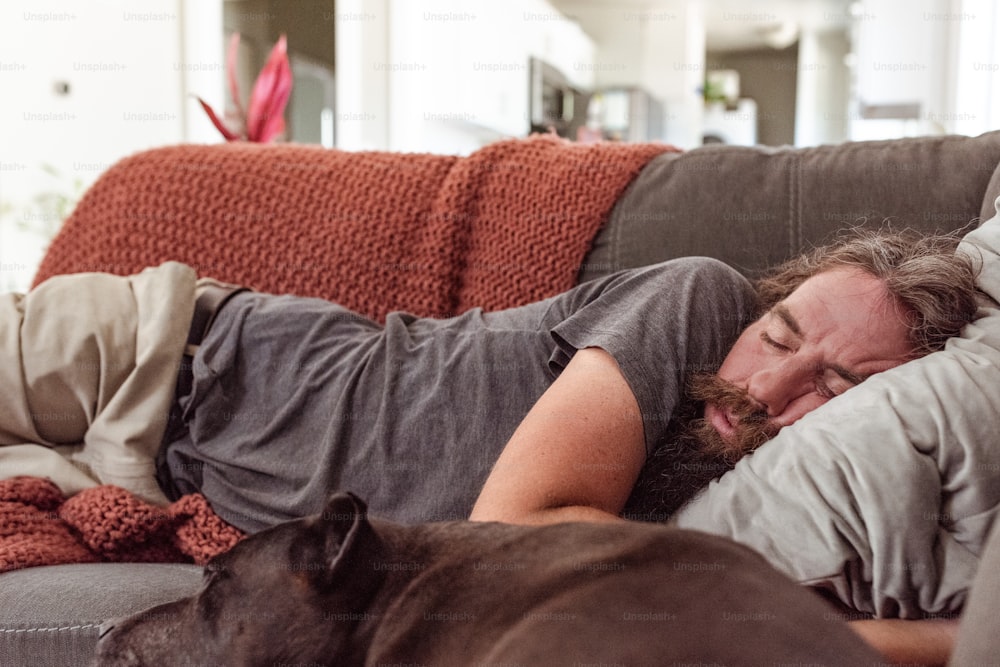 a man laying on a couch next to a dog