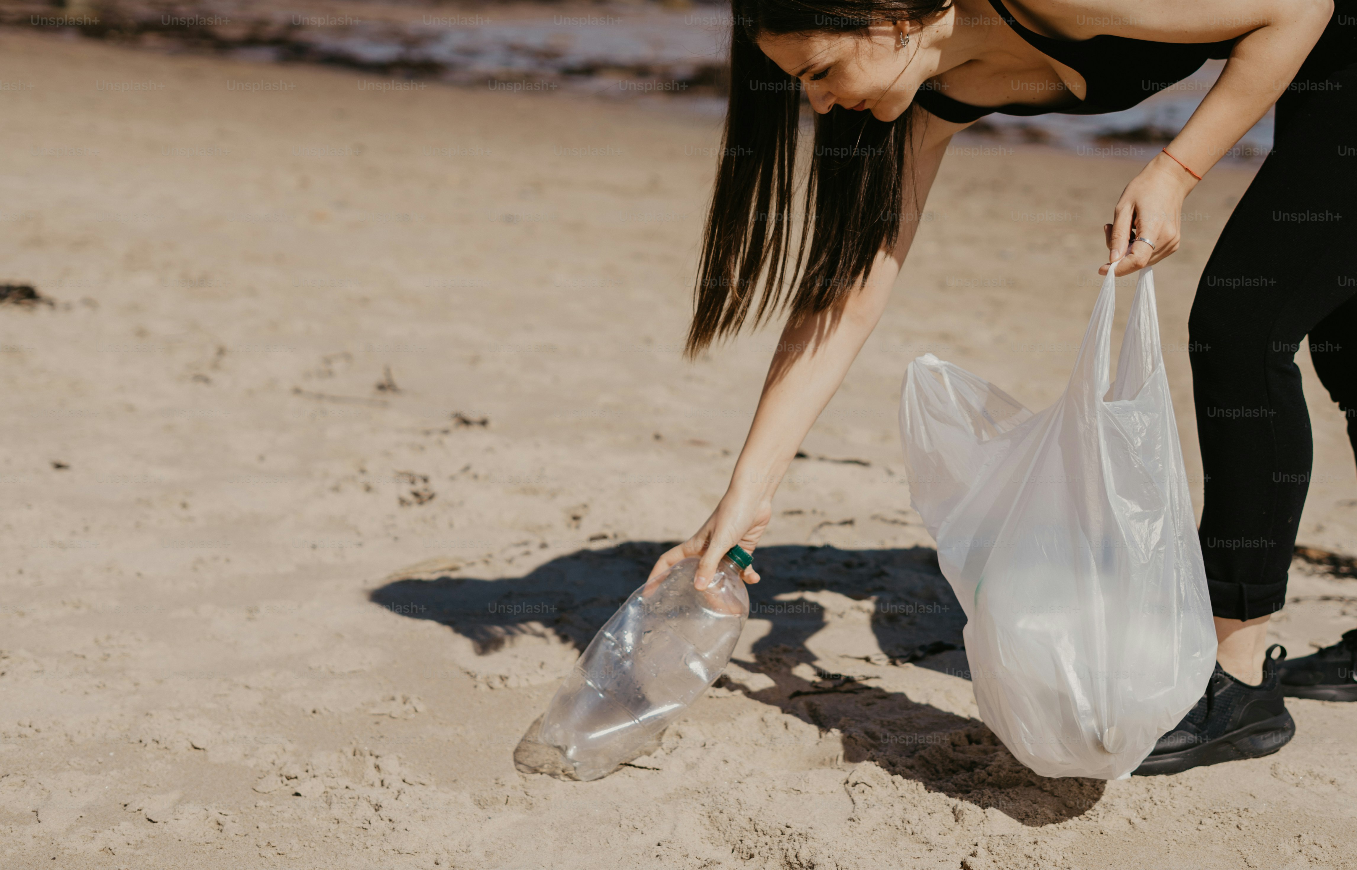 A woman picking up a plastic bag on the beach photo Beach clean up