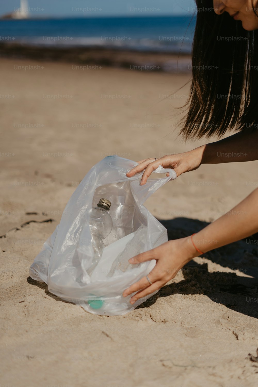 Una donna che raccoglie una bottiglia di plastica dalla sabbia
