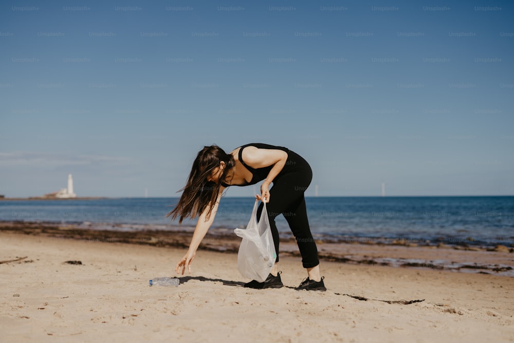 uma mulher curvando-se com um saco em uma praia