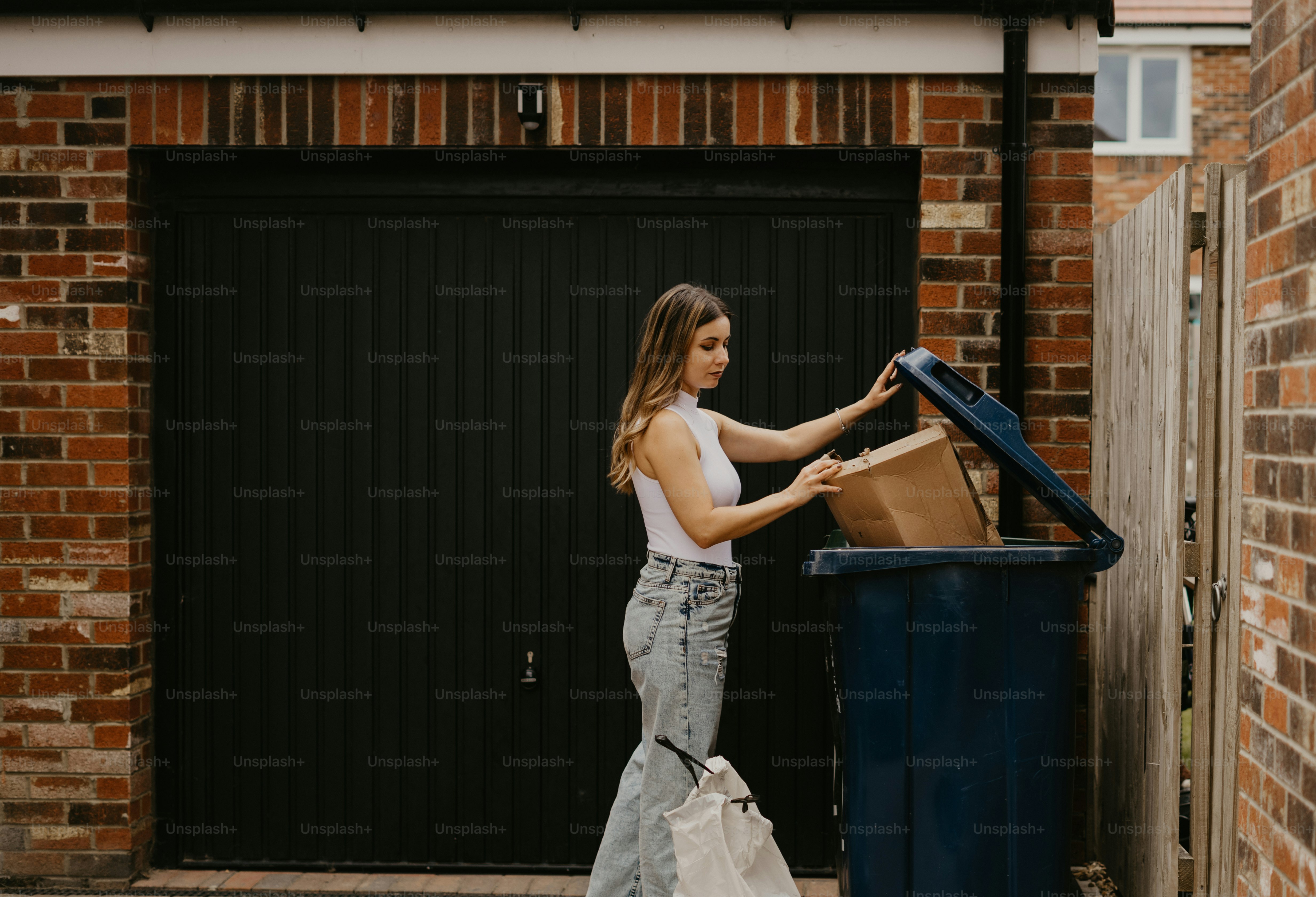 a woman standing next to a blue trash can