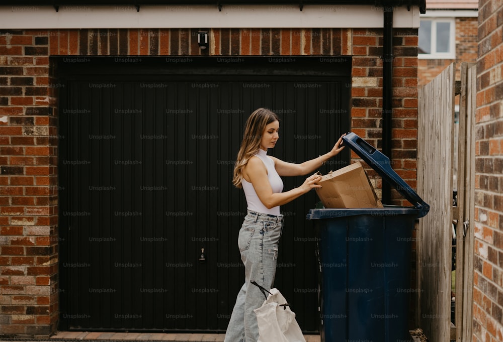 Eine Frau, die neben einem blauen Mülleimer steht