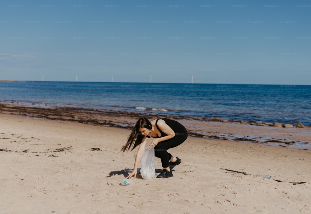 uma mulher ajoelhada em uma praia ao lado do oceano