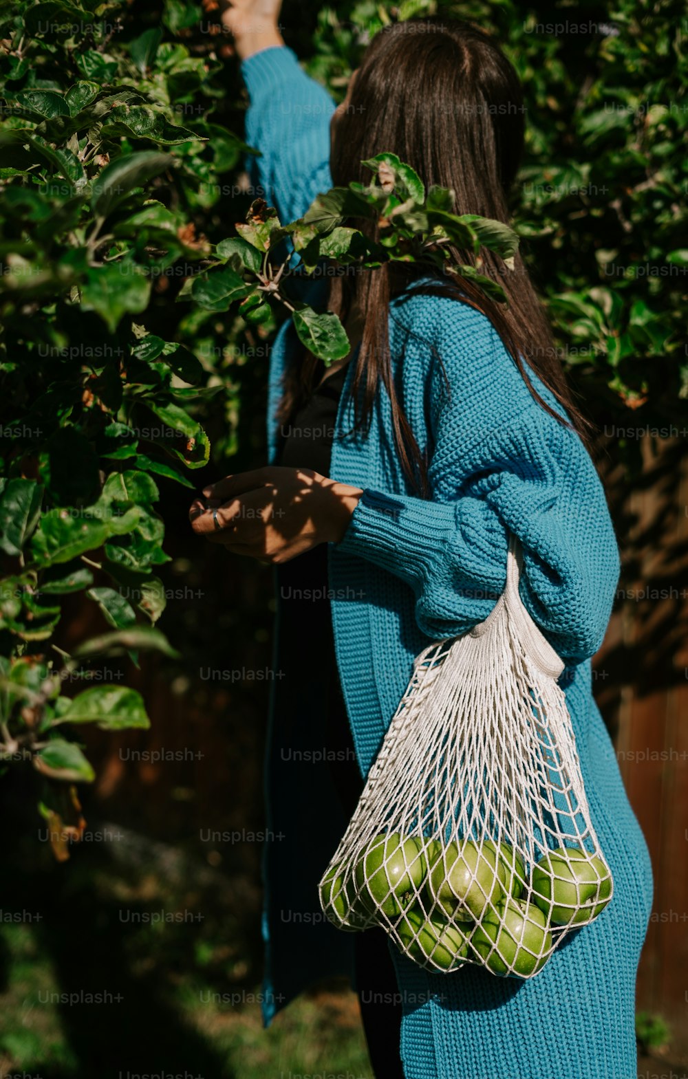a woman in a blue sweater carrying a mesh bag