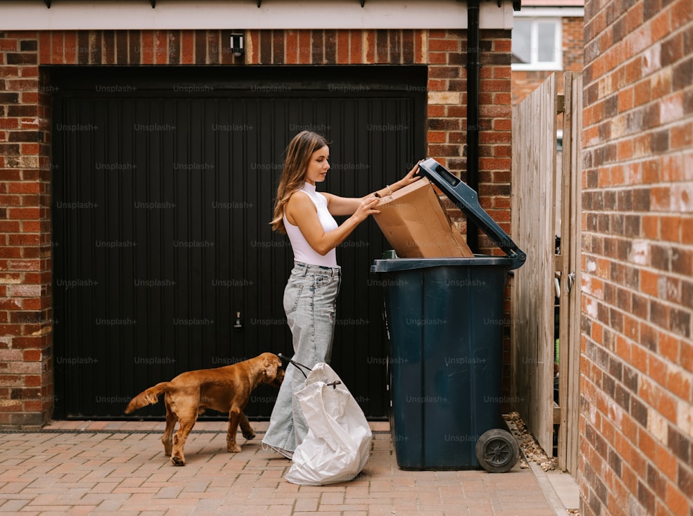 uma mulher ao lado de um cachorro perto de uma lata de lixo