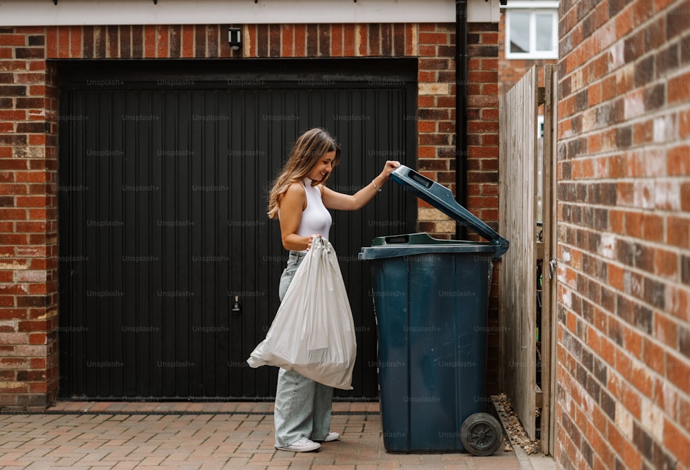 Una mujer parada junto a un bote de basura