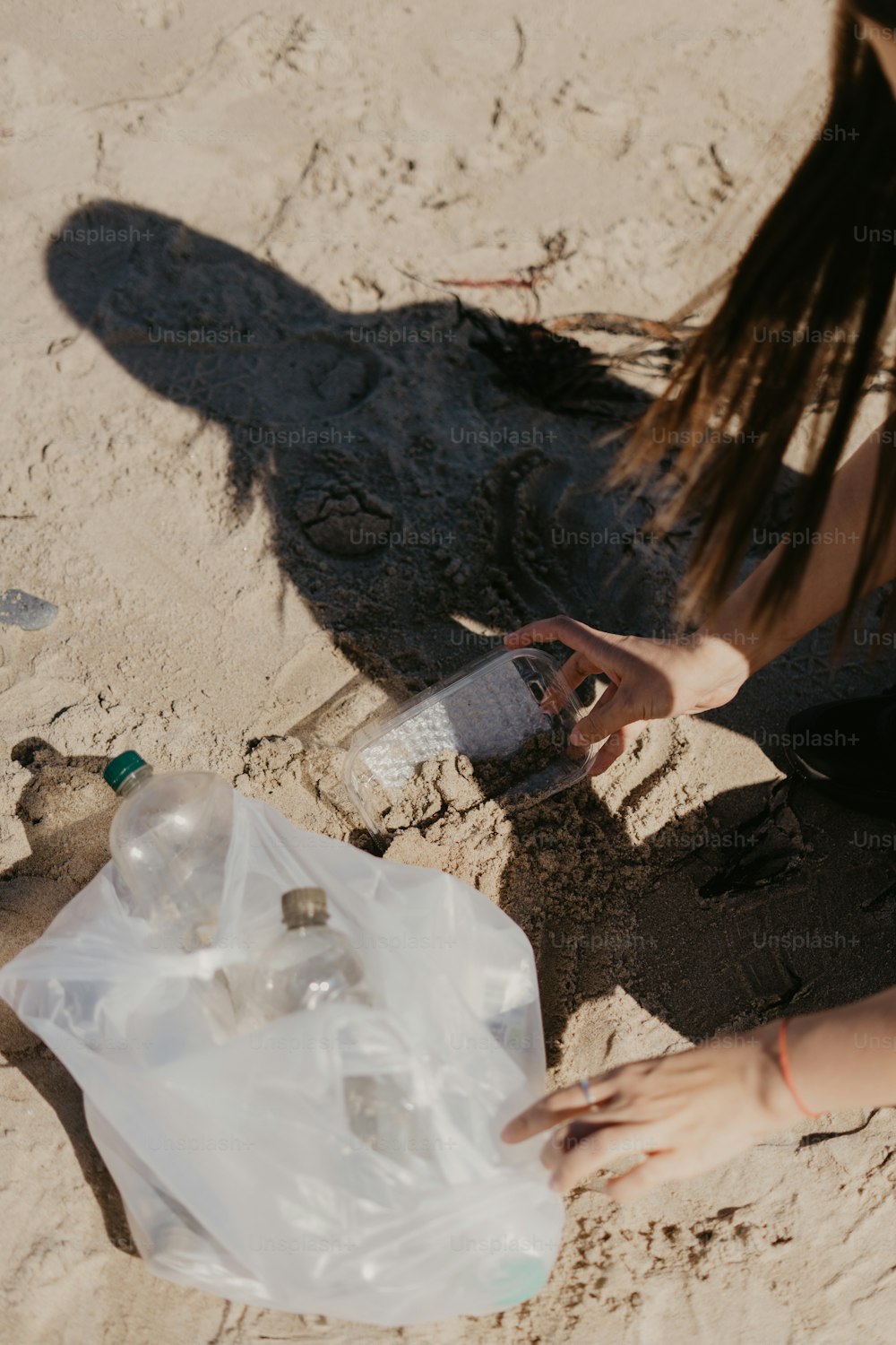 a woman sitting in the sand with a plastic bag