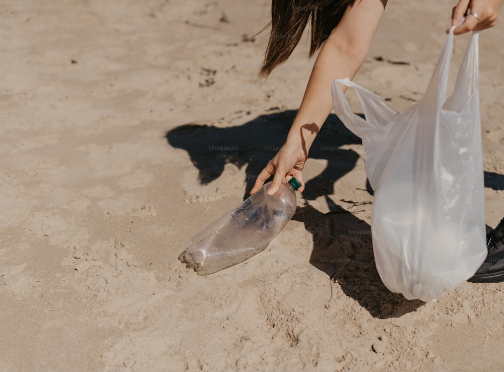 a woman picking up a plastic bag on the beach