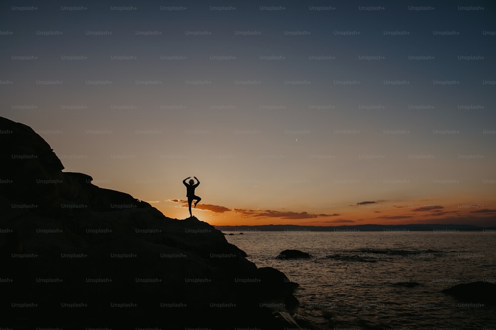 Una persona parada en la cima de una roca junto al océano