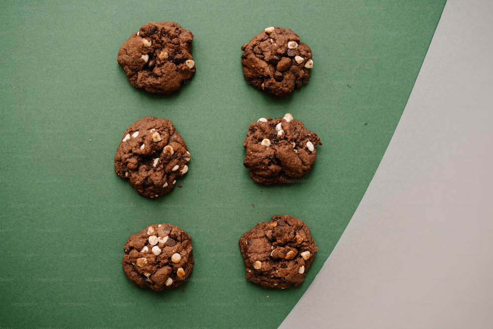 Sechs Schokoladenkekse mit weißen Schokoladenstückchen auf grüner Fläche