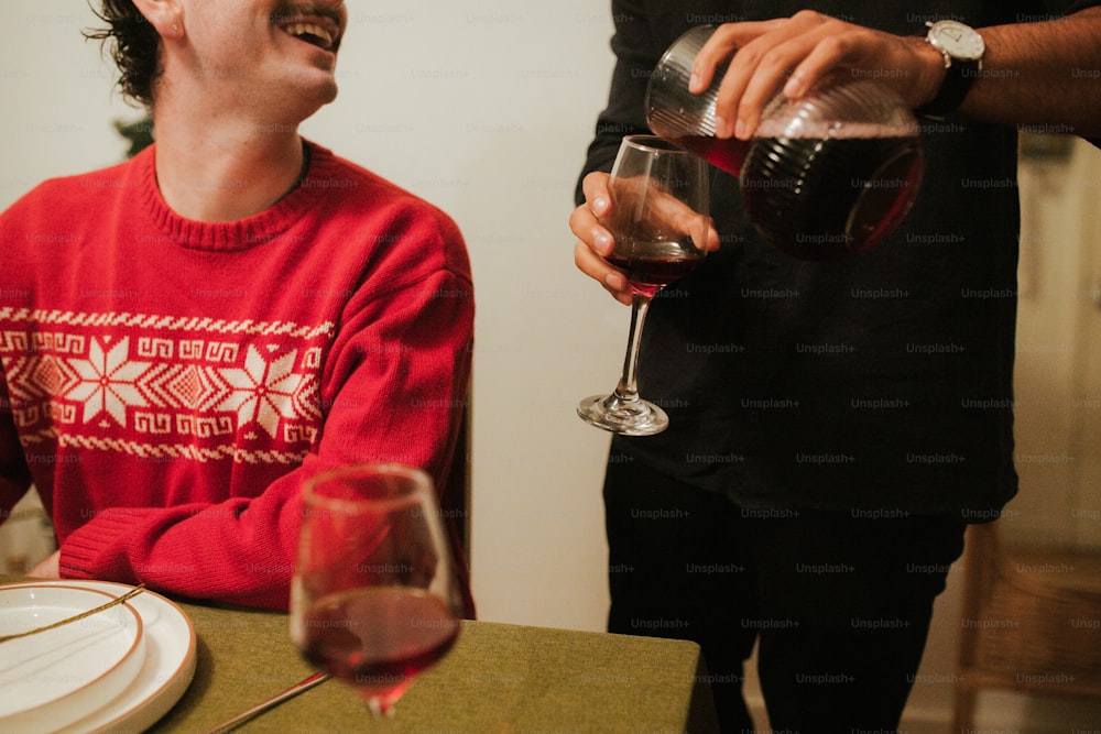 Un uomo in un maglione rosso che versa un bicchiere di vino