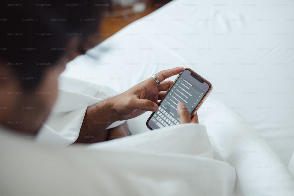eine Person, die auf einem Bett sitzt und auf ein Handy schaut