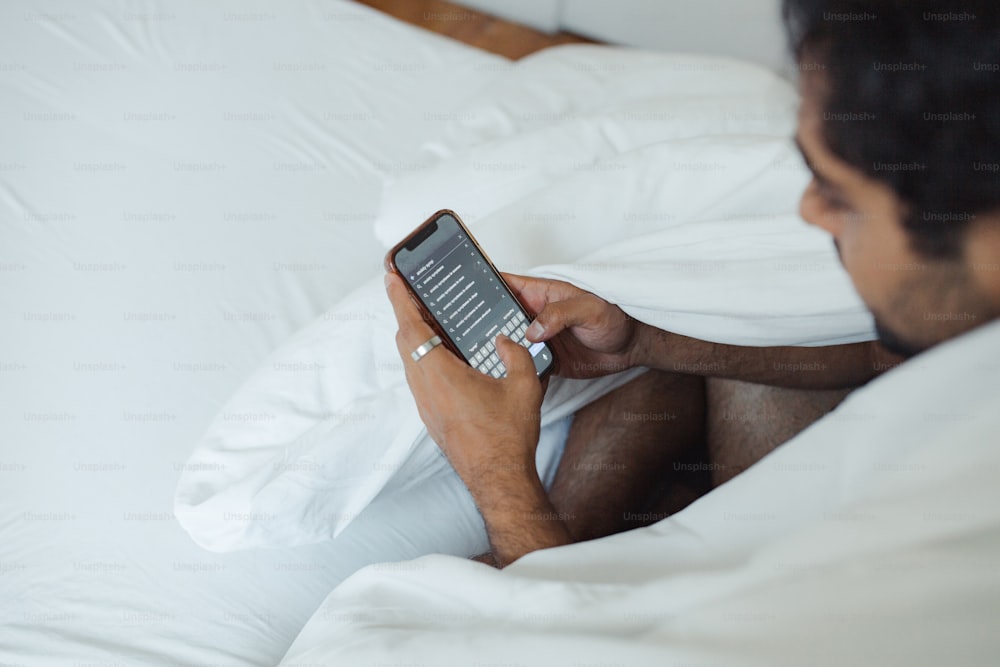 한 남자가 손에 휴대폰을 들고 침대에 누워 있다