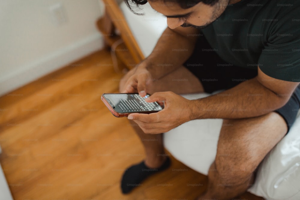 a man sitting on a bed looking at his cell phone