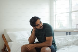 a man sitting on top of a bed next to a window