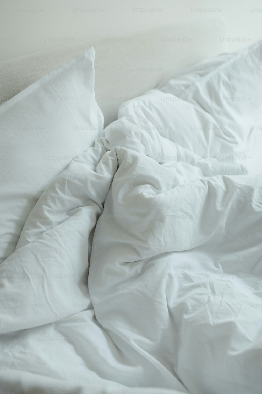 uma cama não feita com lençóis e travesseiros brancos