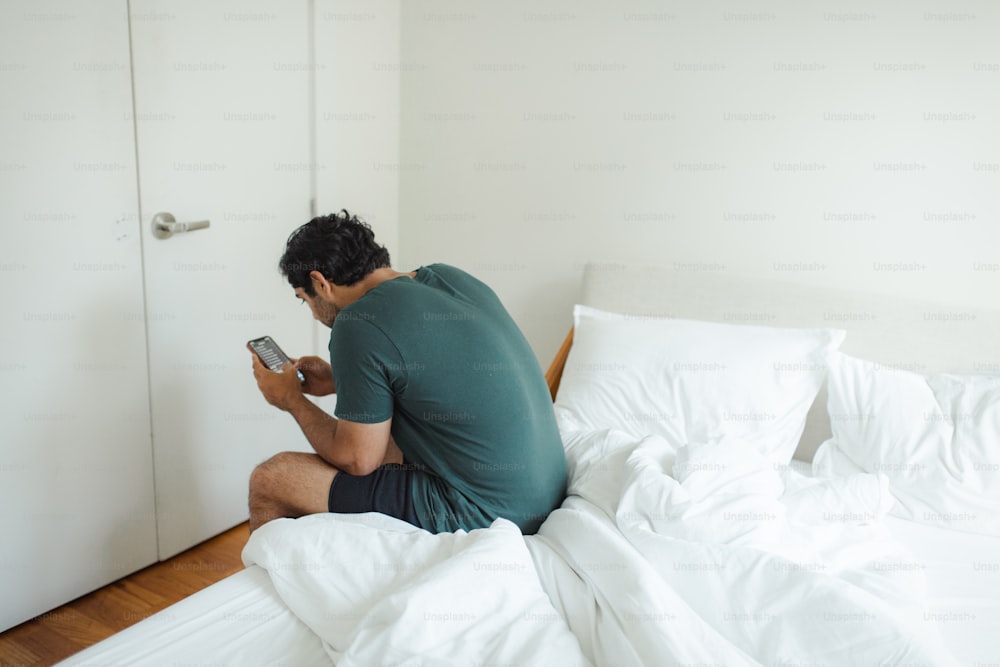 a man sitting on a bed looking at a cell phone