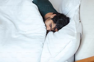 um homem dormindo em uma cama com lençóis brancos