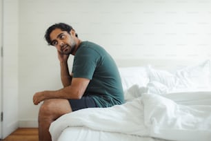 a man sitting on top of a bed talking on a cell phone