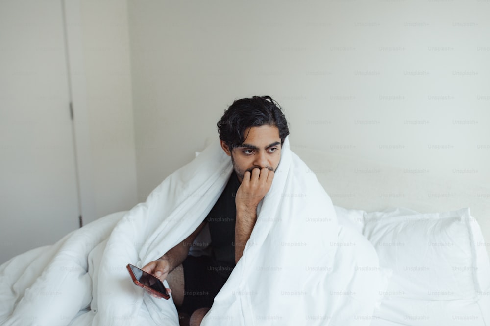 a man sitting on a bed covered in a blanket