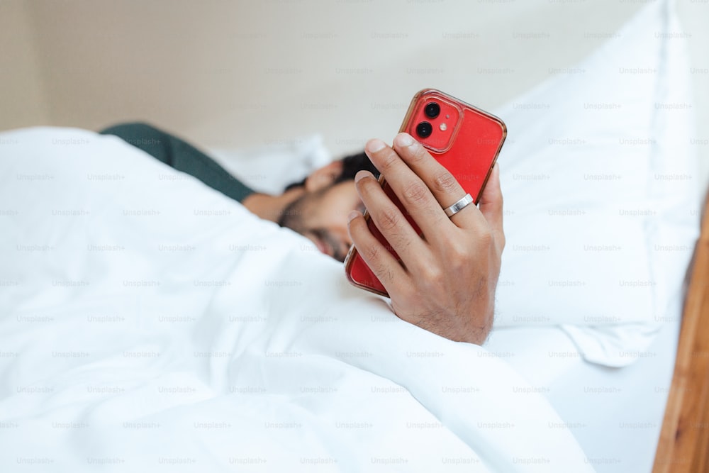 a man laying in bed holding a red cell phone