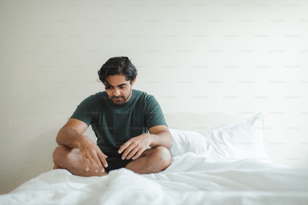 Un hombre sentado en una cama con sábanas blancas