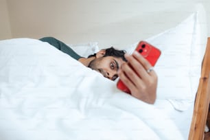 um homem deitado na cama olhando para um celular