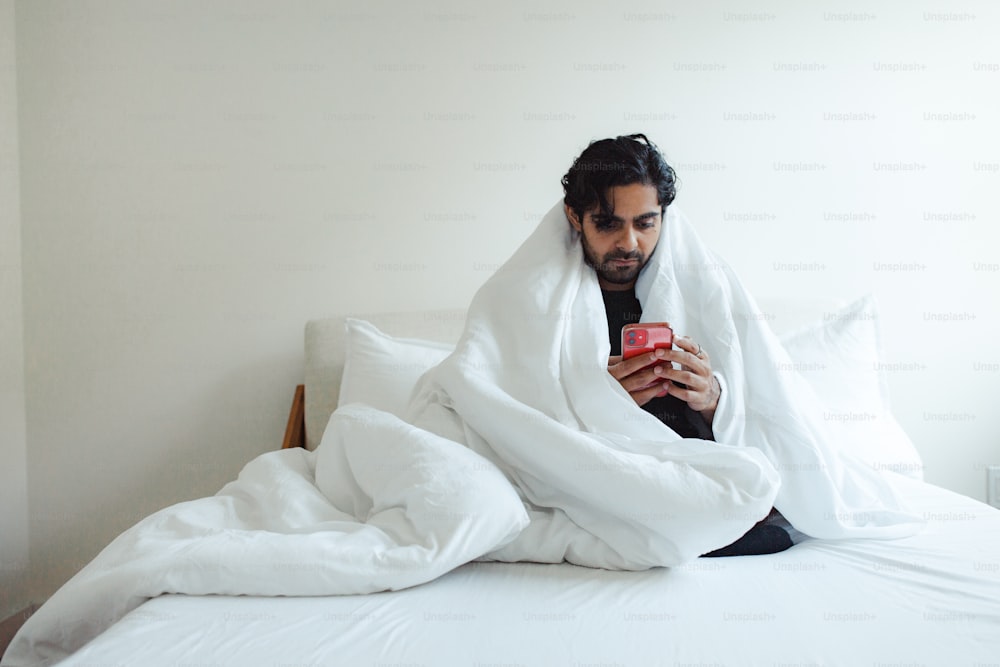 um homem sentado em uma cama olhando para um celular