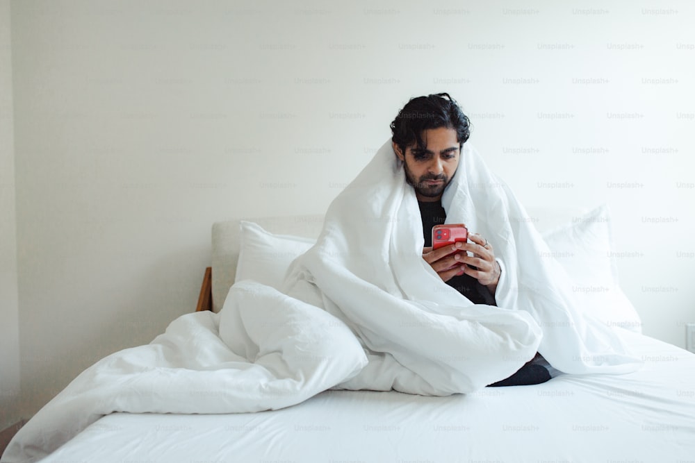 Un hombre sentado en una cama mirando un teléfono celular