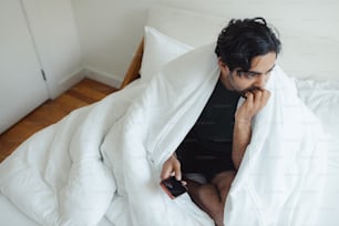 um homem sentado em uma cama enrolado em um cobertor