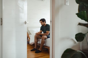 a man sitting on a bed looking at his cell phone