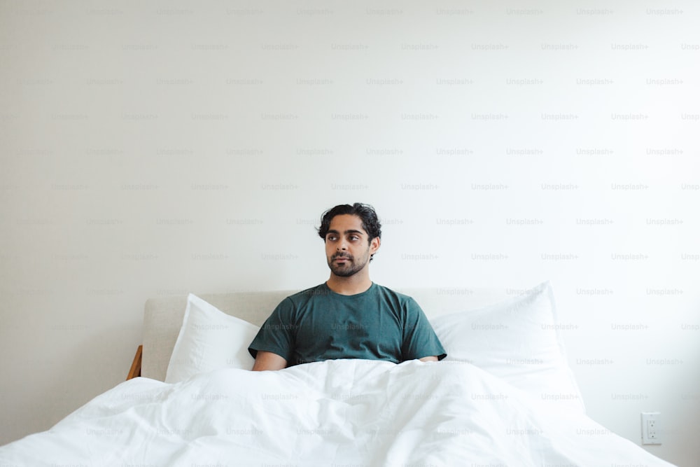 a man sitting on a bed with white sheets