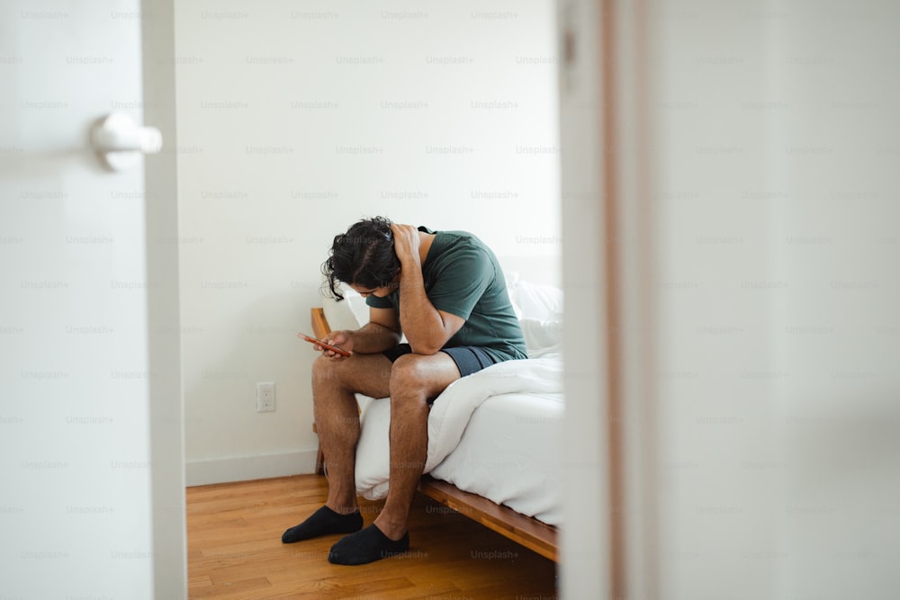 un uomo seduto su un letto con la testa tra le mani