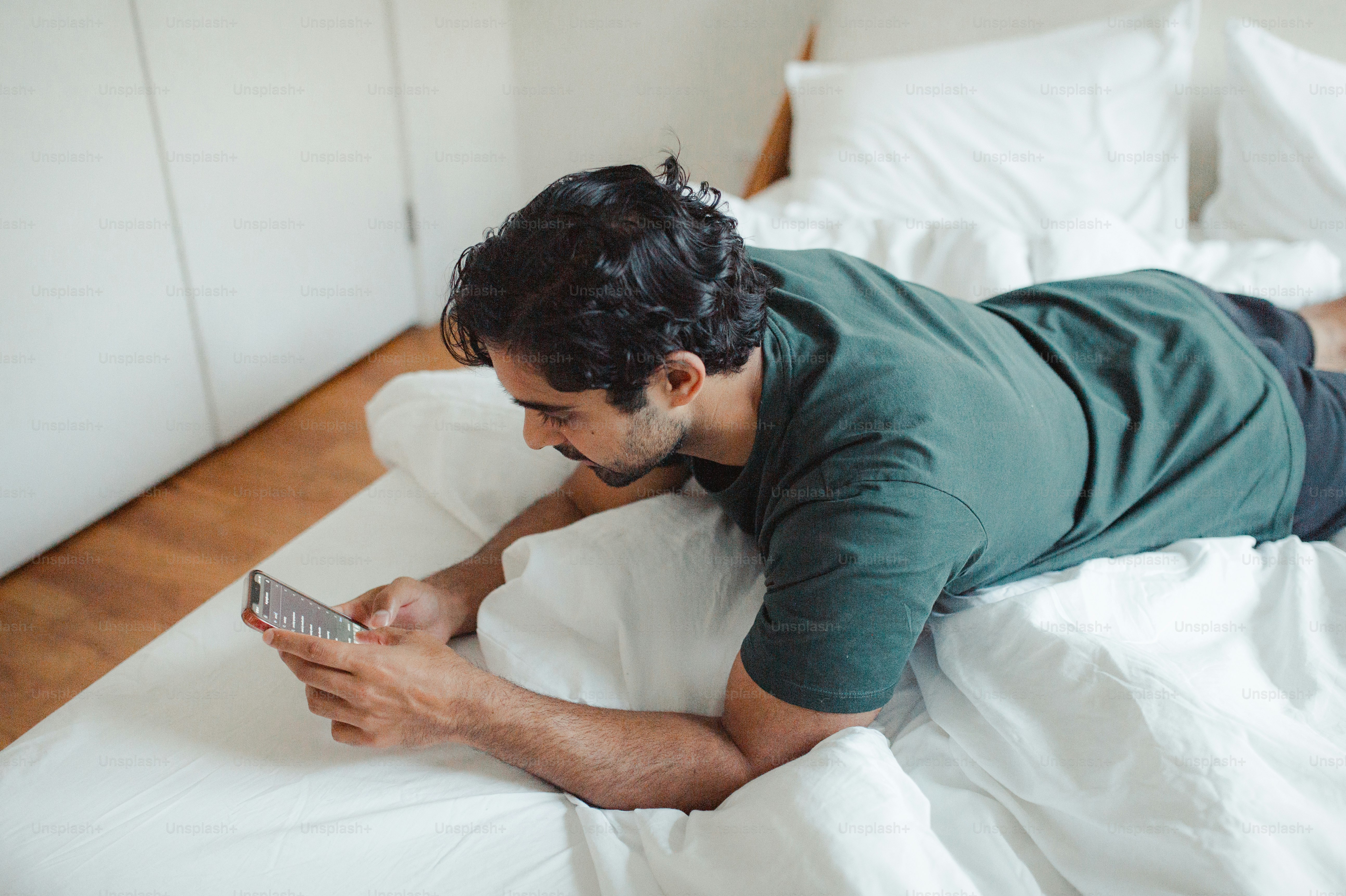 Un hombre acostado en una cama mirando un teléfono celular
