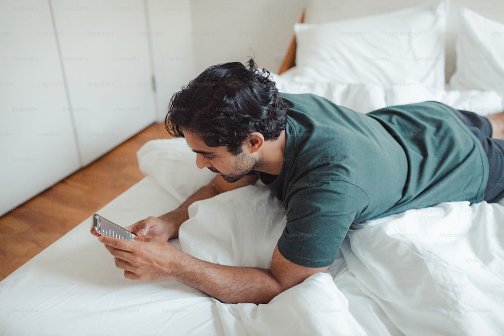 a man laying on a bed looking at a cell phone