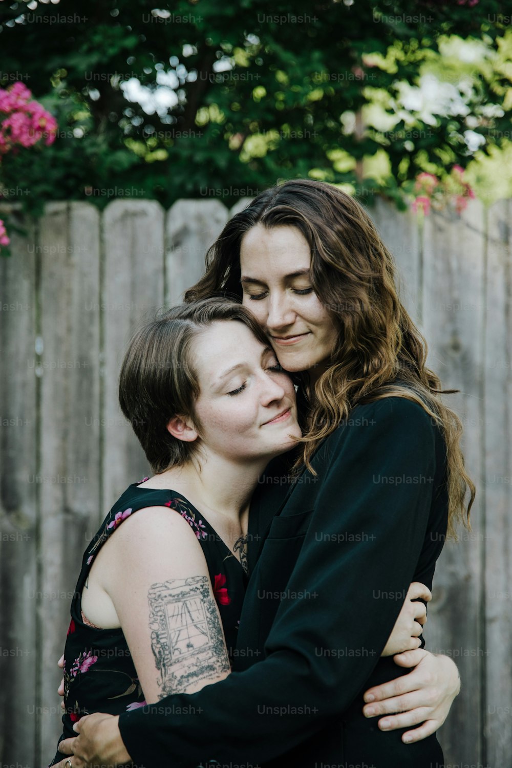 duas mulheres se abraçando em frente a uma cerca