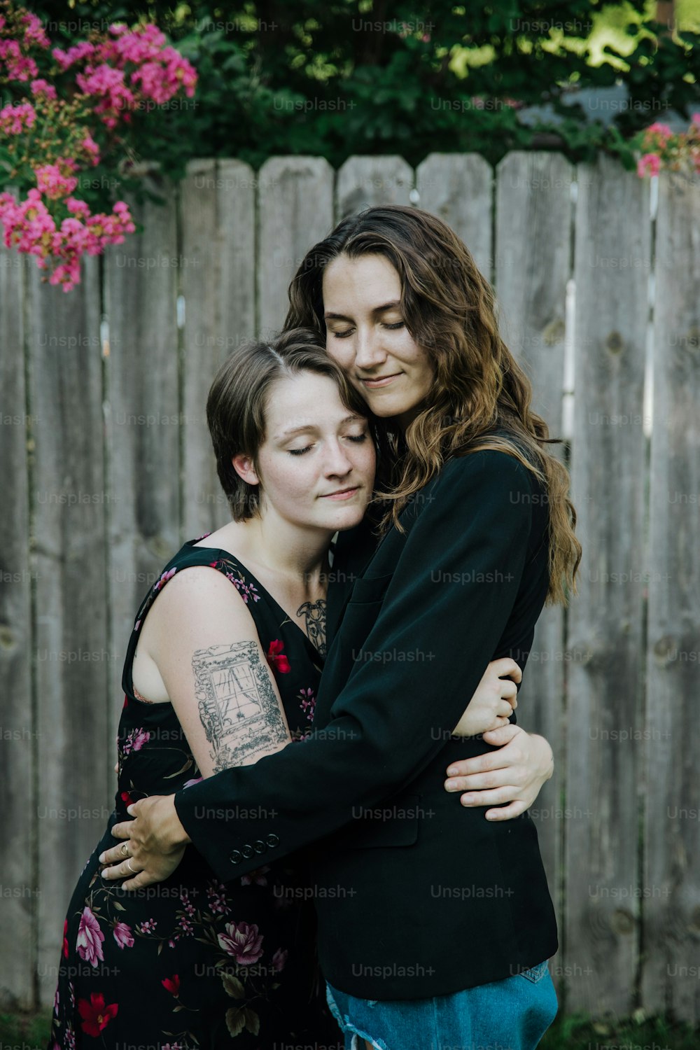 duas mulheres se abraçando em frente a uma cerca