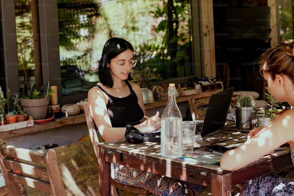 two women sitting at a table with a laptop